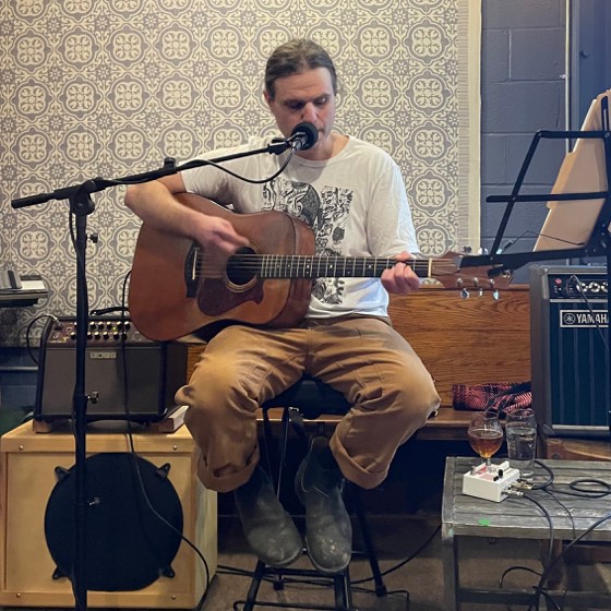 Mike Luz playing acoustic guitar and singing into a microphone at a show